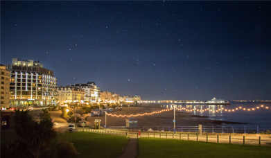 Overlooking Eastbourne seafront at night with a starry dark sky and pier in the distance with strings of white lights along the promenade